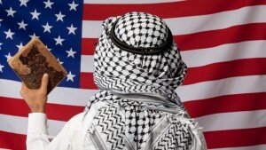 Person wearing Keffiyeh and holding a Quran facing American flag