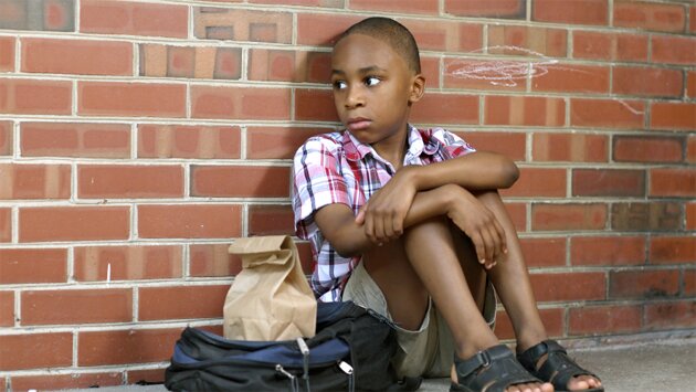 Small boy sitting on the ground with his backback and bag lunch