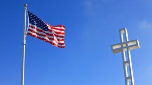 A U.S. flag and a cross against a blue sky