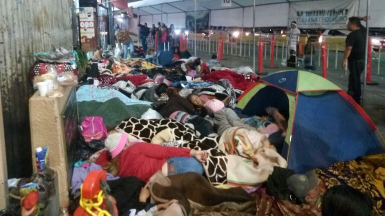 Crowd of people huddled together, sleeping on the ground at the U.S.-Mexico border.