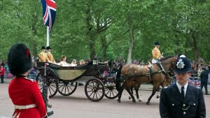 A police officer and a member of the British Royal Guard in the foreground, a horse-drawn carriage in the background