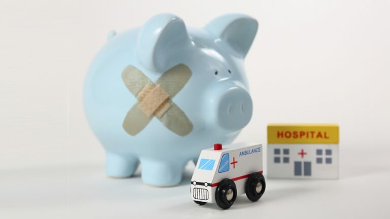 A piggy bank with 2 bandaids on it stands next to a toy hospital and a toy ambulance