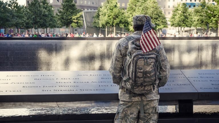 Soldier in field uniform with a U.S. flag on his backpack stands at the 9/11 memorial in NYC
