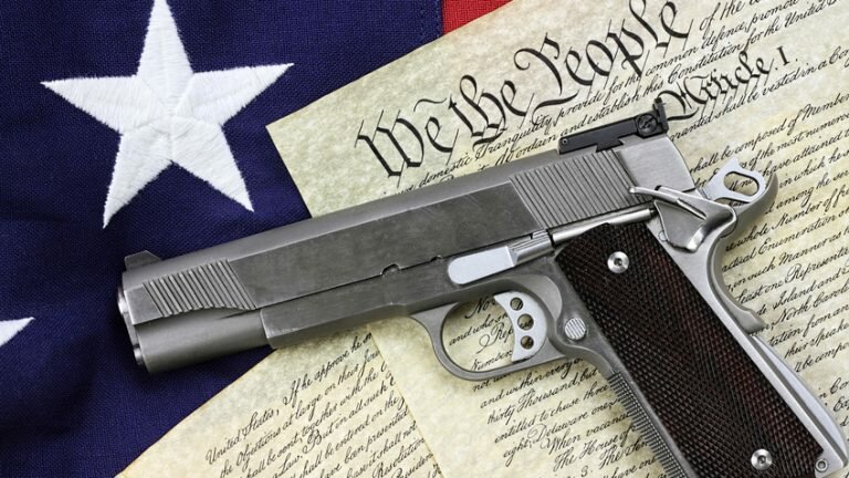 A handgun sits on a copy of the Constitution and the U.S. flag